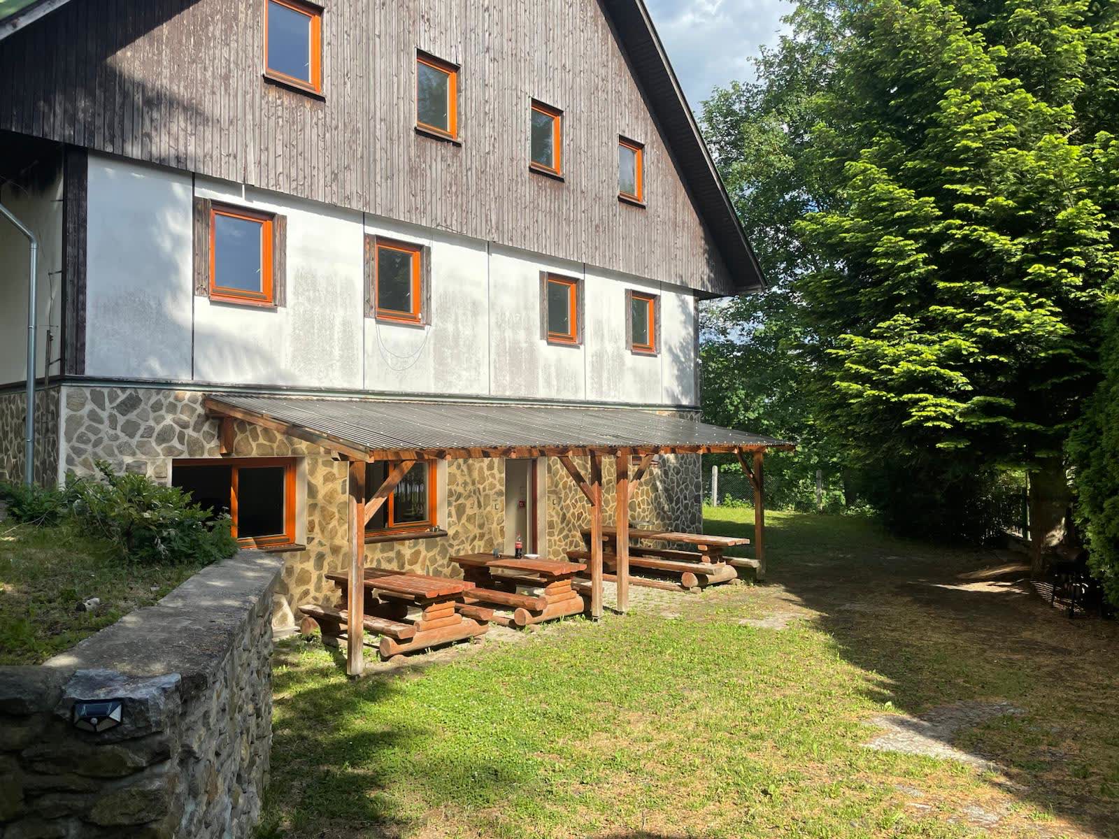 Krytá pergola s kládovými lavicemi před chatou